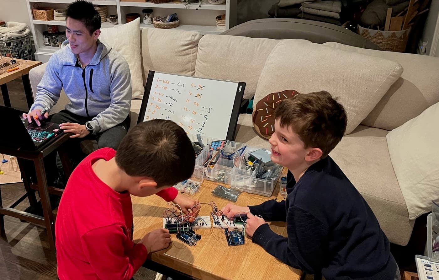 A tutor building electronics projects with two kids at a coffee table
